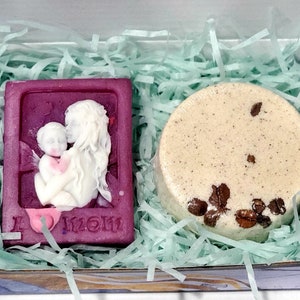 May include: A gift box filled with green shredded paper containing a purple soap bar with a white relief design of a mother and child and the text "I love mom" and a round beige soap bar with brown flecks.