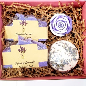 May include: A pink gift box filled with lavender-scented bath products. The box contains two bars of lavender soap, a bath bomb, and a lavender-colored rose. The soap bars are labeled "Relaxing Lavender Natural Soap".