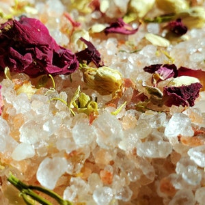May include: Close-up of pink Himalayan salt bath soak with dried rose petals and white jasmine flowers.