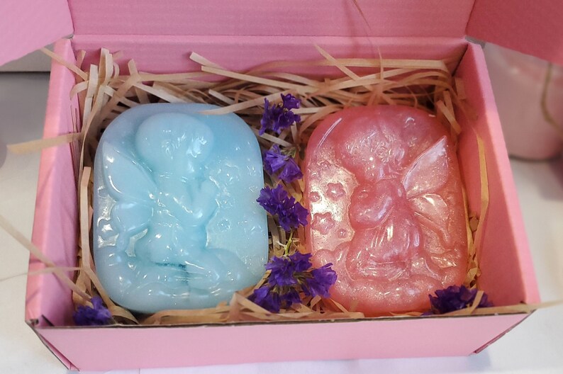 May include: Two small fairy-shaped soaps in a pink gift box. One soap is light blue and the other is pink with glitter.