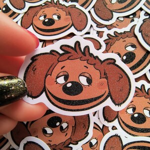 May include: A stack of brown and white dog face stickers with glitter. The dog has a brown face with a black nose and eyes. The dog is smiling.