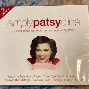 May include: A two-disc CD set featuring Patsy Cline, known as the "first lady of country". The front cover features a color photo of Patsy Cline in a red and white dress, with the title "simply patsycline" in red text. The album includes songs such as "Crazy", "A Poor Man's Roses", "Three Cigarettes In An Ashtray", "Walkin' After Midnight", "Lovesick Blues", "Strange", and "I Fall To Pieces".