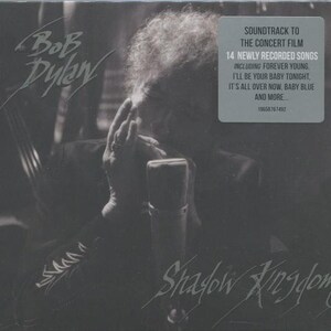 May include: A black and white album cover for "Shadow Kingdom" by Bob Dylan. The image features a close-up of Dylan with a microphone. The album cover includes text that reads "SOUNDTRACK TO THE CONCERT FILM" and lists song titles.