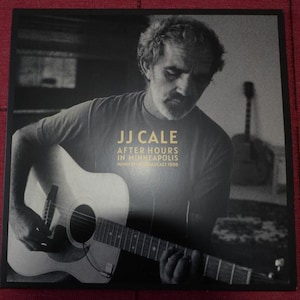 May include: Album cover featuring JJ Cale, playing an acoustic guitar. The text reads "JJ Cale After Hours in Minneapolis Minnesota Broadcast 1998" in gold lettering. The image is a black and white photograph.