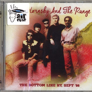 May include: A promotional image for a music album by Bruce Hornsby and The Range. The album cover features a photo of the band members against a red and yellow background. The album title "The Bottom Line HY, Sept '86" is printed at the bottom of the image.