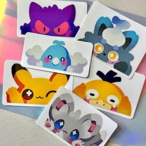Puede incluir: Una colección de pegatinas coloridas con personajes de dibujos animados. Las pegatinas muestran varios diseños, incluyendo un fantasma morado, un koala azul, un Pikachu amarillo y otras criaturas lindas y expresivas. Cada pegatina tiene un borde blanco.