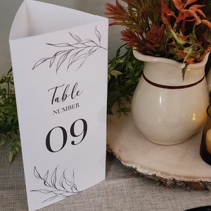 May include: White table number card with black calligraphy that says "Table Number 09" and a black line drawing of leaves.