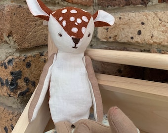 May include: A white and brown stuffed deer toy with brown spots. The deer is sitting on a small, floral patterned suitcase.