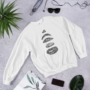 Peut inclure: Sweat-shirt blanc avec un motif graphique noir représentant une pile de cinq cercles superposés avec un motif texturé.