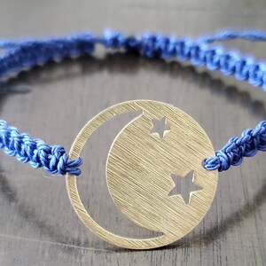 Puede incluir: Una pulsera trenzada azul con un dije dorado con forma de luna creciente y dos estrellas.