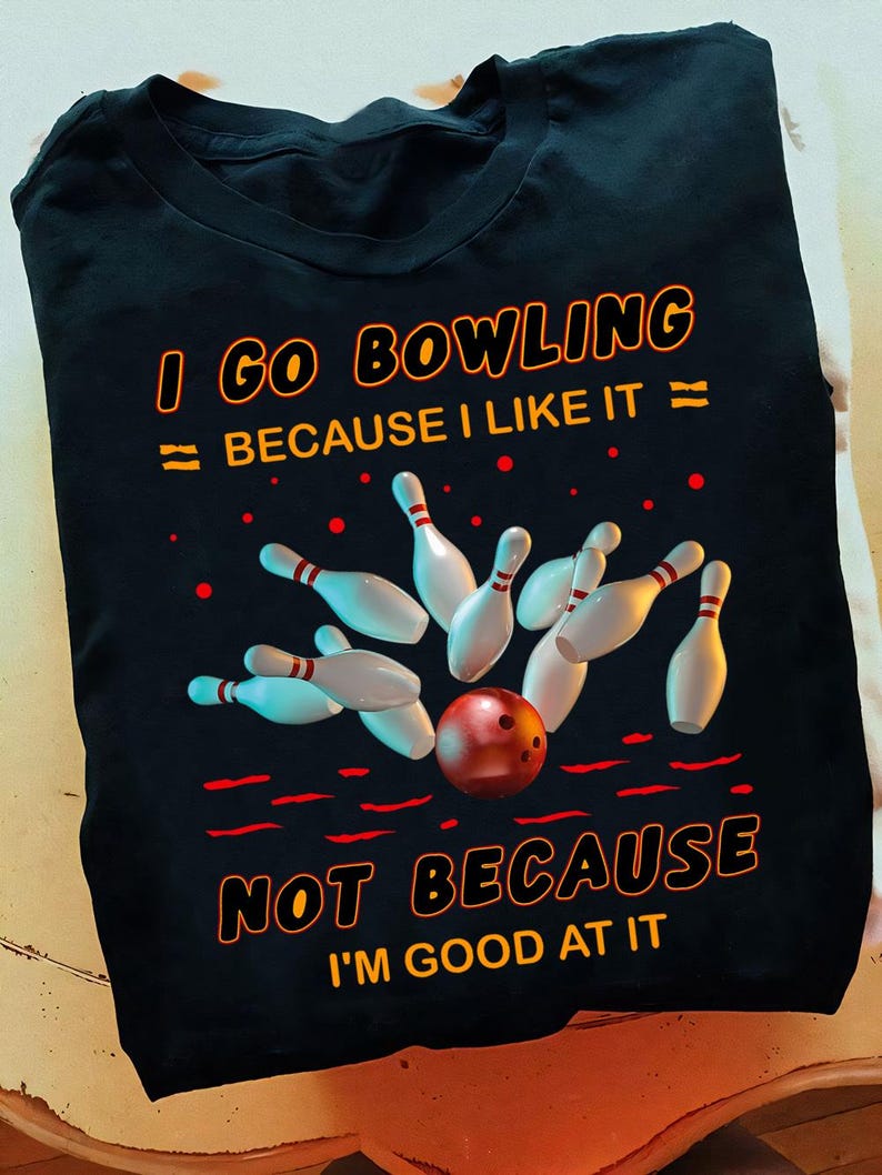 K&ouml;nnte beinhalten: Schwarzes T-Shirt mit einem Bowling-Motiv. Das Motiv zeigt eine Bowlingkugel und Pins mit dem Text "Ich gehe Bowling, weil ich es mag, nicht weil ich gut darin bin."