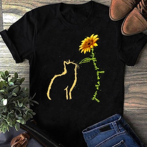 K&ouml;nnte beinhalten: Schwarzes T-Shirt mit einer Silhouette einer Katze, die zu einer gelben Sonnenblume mit dem Text "you are my sunshine" in Gr&uuml;n schaut.