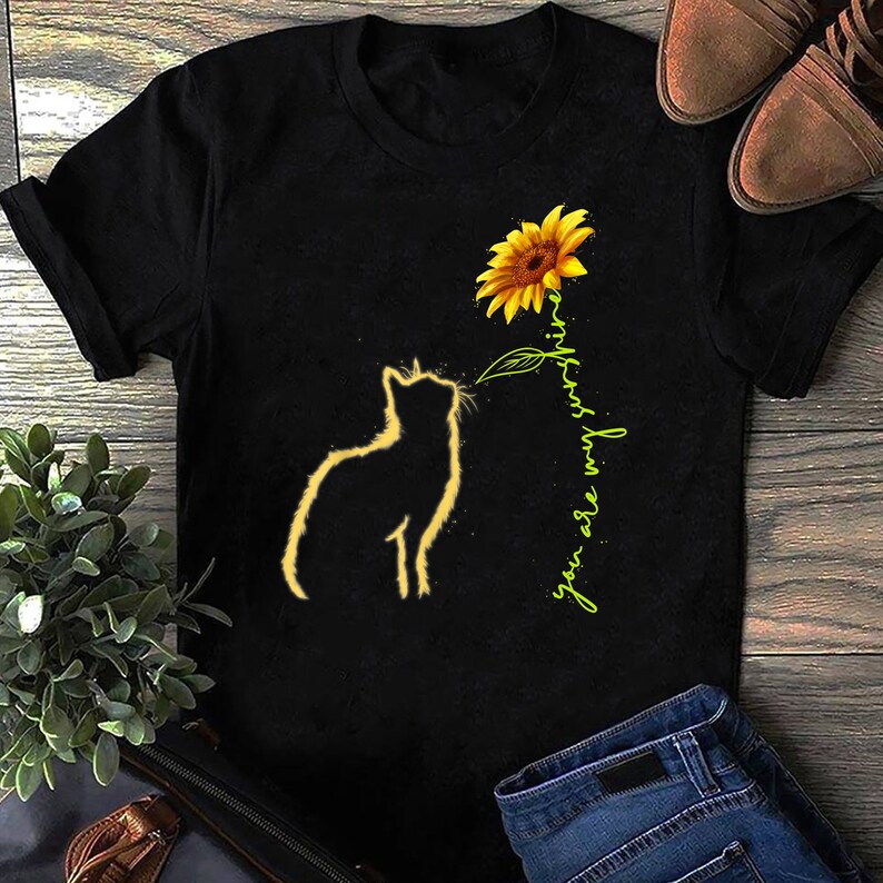 K&ouml;nnte beinhalten: Schwarzes T-Shirt mit einer Silhouette einer Katze, die zu einer gelben Sonnenblume mit dem Text "you are my sunshine" in Gr&uuml;n schaut.