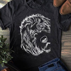 Op de afbeelding: Een zwart T-shirt met een witte lijntekening van een hondenkop. De hond heeft pluizig haar en kijkt naar rechts.