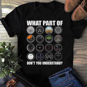 May include: Black t-shirt with the text "WHAT PART OF DON'T YOU UNDERSTAND?" above a grid of aviation instrument gauges. The shirt is made of a dark fabric and features a crew neck. The design is printed in white.