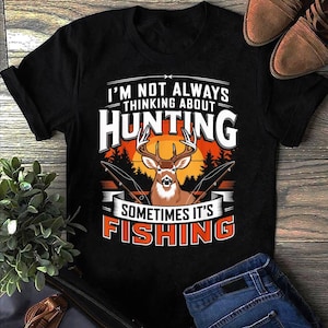 May include: Black t-shirt with a deer graphic and the text "I'M NOT ALWAYS THINKING ABOUT HUNTING SOMETIMES IT'S FISHING". The graphic includes a deer, fishing rods, and a sunset.