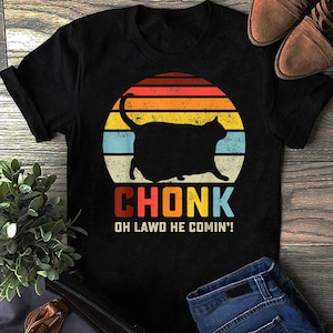 May include: Black t-shirt with a retro-style sunset graphic featuring a cartoon cat with the text "CHONK OH LAWD HE COMIN'!".