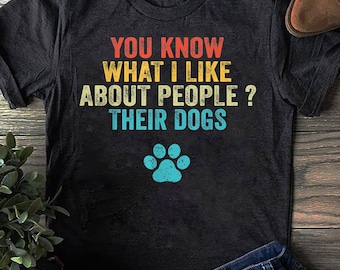 Może przedstawiać: Czarny T-shirt z grafiką w stylu vintage, na której widnieje napis "You know what I like about people? Their dogs." Grafika jest w kolorze czerwonym, żółtym i niebieskim. Pod tekstem znajduje się niebieski ślad łapy.