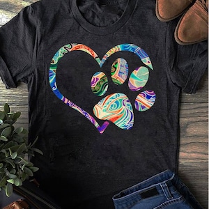 May include: A dark gray t-shirt with a colorful paw print inside a heart design. The paw print and heart are filled with swirling patterns in shades of blue, green, purple, orange, and white.