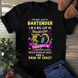 Könnte beinhalten: Schwarzes T-Shirt mit dem Text "I'M NOT JUST A BARTENDER I'M A BIG CUP OF Wonderful COVERED IN AWESOME SAUCE WITH A SPLASH OF SASSY AND A DASH OF CRAZY". Das Design beinhaltet einen Cocktailshaker und florale Elemente.