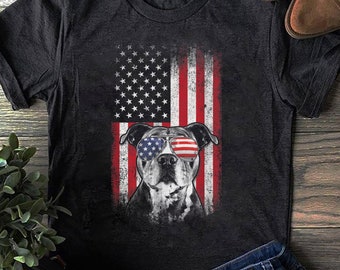 May include: A black t-shirt with a distressed American flag design featuring a pit bull wearing red, white, and blue sunglasses.