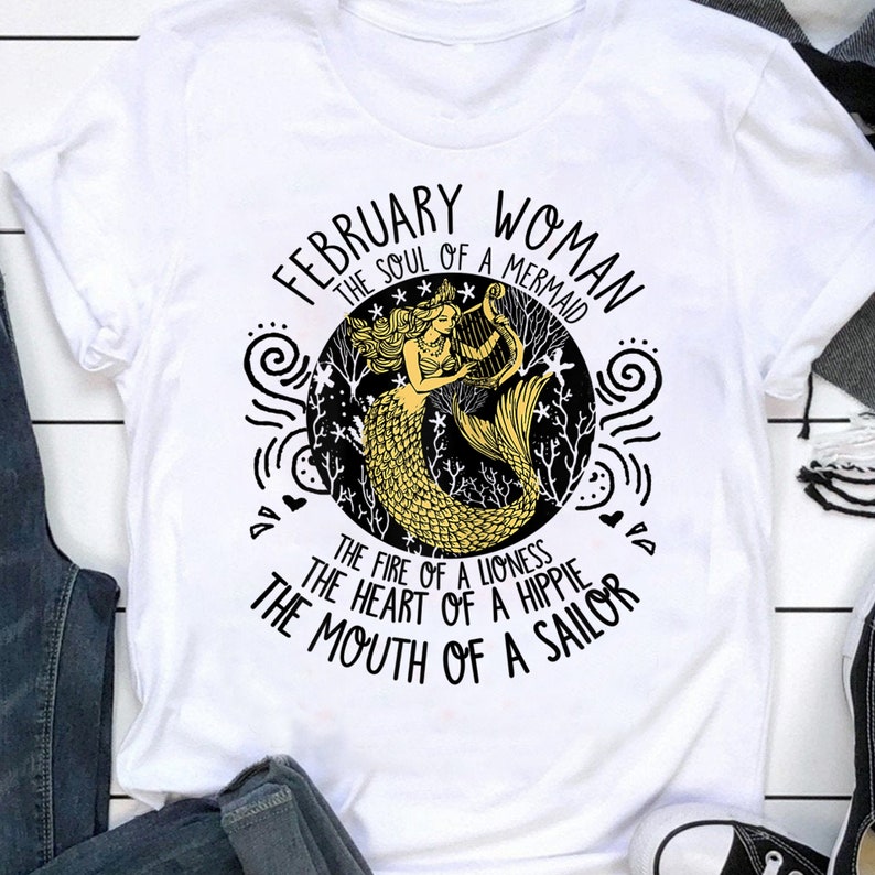 May include: White t-shirt with a black and gold graphic design featuring a mermaid playing a harp. The text reads "February Woman The Soul of a Mermaid The Fire of a Lioness The Heart of a Hippie The Mouth of a Sailor"