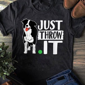 Peut inclure: Un chien border collie noir et blanc avec la langue rouge qui sort, debout sur un t-shirt gris foncé avec le texte "JUST THROW IT" en lettres blanches.