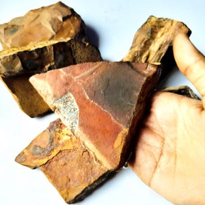 Puede incluir: Una colección de rocas rugosas de forma irregular en tonos marrones, rojos y beige. Las rocas tienen un aspecto natural y texturizado, con variaciones de color y patrón. La imagen está bien iluminada, destacando los detalles de la piedra.