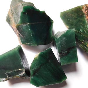 Puede incluir: Un conjunto de piedras de jade verdes en bruto, sin cortar. Las piedras varían en tamaño y forma, con un color verde intenso y texturas naturales visibles. Algunas piezas tienen inclusiones marrones y negras.