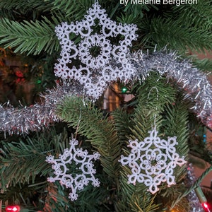 May include: Three white crocheted snowflakes hanging on a Christmas tree with silver tinsel. The snowflakes are delicate and intricate, with a star-shaped design. The text "Three tatting snowflakes by Melanie Bergeron" is visible at the top of the image.