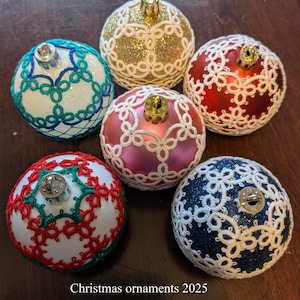 Peut inclure: Six boules de Noël avec des motifs de dentelle complexes. Les boules sont de différentes couleurs, dont l'or, le rouge, le bleu, le rose et le vert, avec des paillettes. Le texte "Christmas ornaments 2025 by Mélanie Bergeron" est en bas.