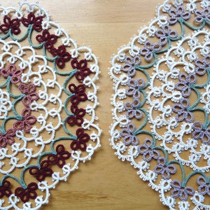 Peut inclure: Deux napperons en crochet blanc avec des motifs complexes. Un napperon a un schéma de couleurs bordeaux et vert, tandis que l'autre a un schéma de couleurs violet et vert.