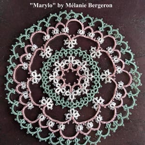 May include: A handmade, circular doily featuring intricate lace patterns. The design incorporates concentric rings of white, pale pink, and mint green thread, creating a delicate floral motif. The text "Marylo" by Mélanie Bergeron is visible.