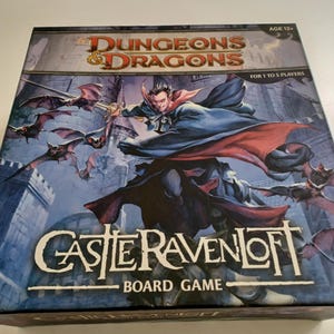 Puede incluir: Una caja de juego de mesa de Dungeons & Dragons con un fondo azul oscuro, un castillo blanco y un vampiro volando en el aire. La caja tiene el título "Castle Ravenloft" y el texto "Board Game" impreso en ella. El juego es para 1 a 5 jugadores y se recomienda para mayores de 12 años.