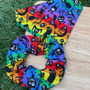 Könnte beinhalten: Ein regenbogenfarbener Haargummi mit einem schwarz-weißen Muster aus Comic-Monster. Der Haargummi ist aus Stoff und hat eine gefaltete Optik.