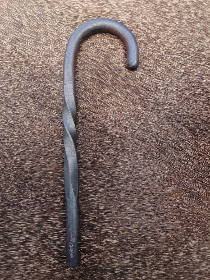 May include: A twisted metal hook with a rounded handle. The hook is made of dark metal and has a rustic appearance.