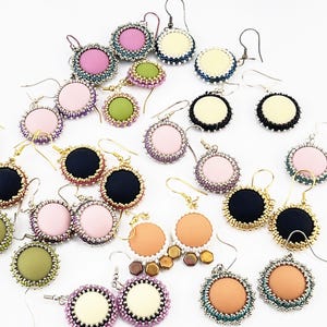 May include: A selection of handmade round earrings in various colours, including pink, black, green, and orange. Each earring has a beaded border and a contrasting centre, with gold or silver ear wires.