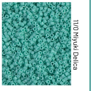May include: Close-up of a pile of turquoise Miyuki Delica seed beads, size 11/0. The cylindrical beads are densely packed, creating a textured surface. The beads are a solid, opaque color, ideal for jewelry making and beadwork.