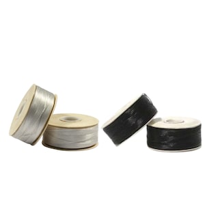 Puede incluir: Dos carretes de hilo plateado y dos carretes de hilo negro. El hilo está enrollado alrededor de carretes de madera.