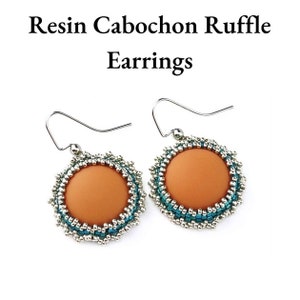 May include: A pair of silver dangle earrings with a peach-colored resin cabochon surrounded by a silver and turquoise beaded ruffle.