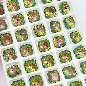 May include: A white tray with square compartments filled with green, iridescent, faceted, square-shaped gemstones.