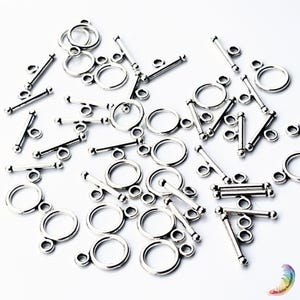 May include: A collection of silver-toned metal toggle clasps for jewelry making, each consisting of a circular ring component and a matching T-bar component, scattered across a plain white background with a small colorful logo in the corner.