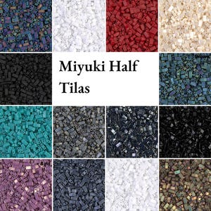 Könnte beinhalten: Eine Auswahl an Miyuki Half Tila Perlen in verschiedenen Farben, darunter Weiß, Rot, Schwarz und schillernde Farbtöne. Die rechteckigen Perlen mit zwei Löchern eignen sich ideal für Schmuckherstellung und Perlenarbeiten.