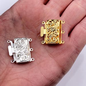Puede incluir: Dos cierres metálicos ornamentados para la elaboración de joyas. Uno es dorado y el otro plateado. Ambos tienen un diseño de filigrana.