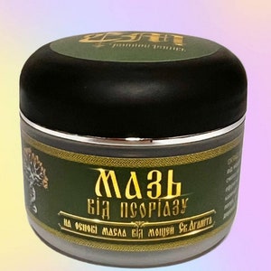 May include: A green and gold jar with a black lid. The jar is labelled "Мазь від псоріазу" which translates to "Ointment for Psoriasis". The label also says "на основі масла від мощен Св. Данита" which translates to "Based on oil from the power of St. Danita".