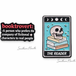 May include: Two enamel pins. One is a black rectangular pin with the text "booktrovert: -A person who prefers the company of fictional characters to real people". The other is a rectangular pin depicting a skull on a stack of books with "THE READER".