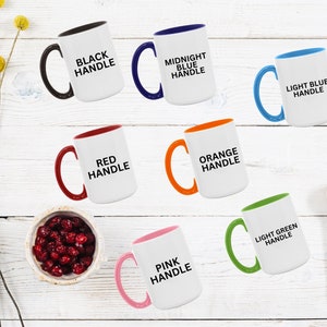 May include: White ceramic mugs with colored handles and the text "BLACK HANDLE", "MIDNIGHT BLUE HANDLE", "LIGHT BLUE HANDLE", "RED HANDLE", "ORANGE HANDLE", "PINK HANDLE", and "LIGHT GREEN HANDLE". A wooden spoon and a bowl of red berries are also present.