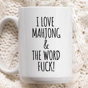 May include: A white ceramic mug with a black handle and the text "But First, Coffee" in a bold, black font. The mug is set against a neutral background, highlighting its simple design.