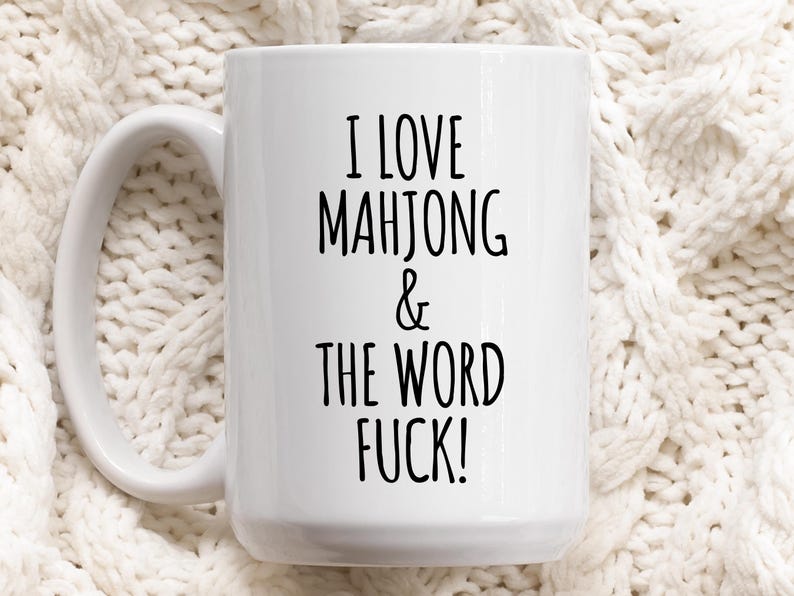 May include: A white ceramic mug with a black handle and the text "But First, Coffee" in a bold, black font. The mug is set against a neutral background, highlighting its simple design.
