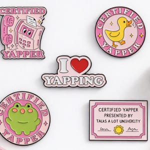 Puede incluir: Cinco pines de esmalte con diseños en rosa y blanco con el texto Certified Yapper, I Love Yapping y un diploma de Talks A Lot University. Los pines incluyen ilustraciones de un teléfono rosa, un pato amarillo y una rana verde.